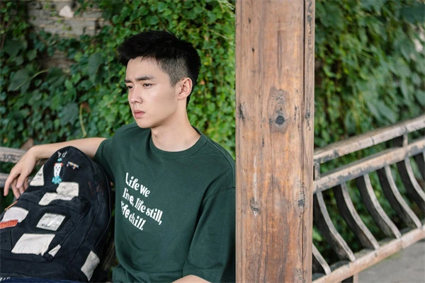 In A Year Without a Job, a young man leans by the post, lost in thought in a green T - shirt.