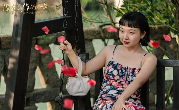 In A Year Without a Job, a woman in a floral dress sits on a swing, surrounded by falling petals.