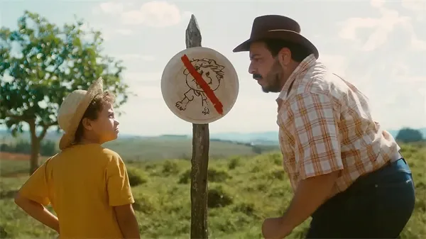 Man and boy face off at a sign in "Chuck Billy e a Goiabeira Maravilhosa".