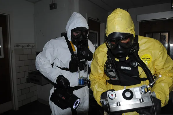 Hazmat - suited team members in "Emergência Radioativa" inspecting equipment.