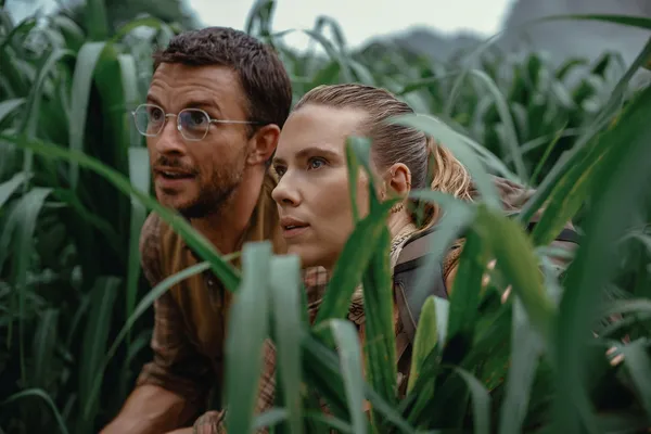 Characters in "Jurassic World Rebirth" hiding amidst tall plants, looking alert.