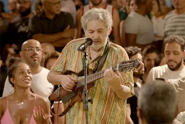 Man performs with guitar in front of crowd in Moacyr Luz, O Embaixador Dessa Cidade.