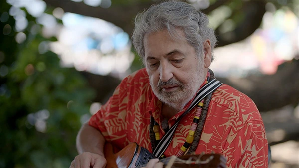 Man plays guitar under a tree in Moacyr Luz, O Embaixador Dessa Cidade.