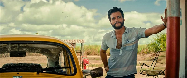 A secret agent stands by a yellow car in a sunlit outdoor setting.