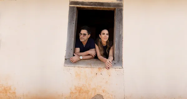 A man and a woman lean out of a simple window in The Family That Sings Together: The Camargos.