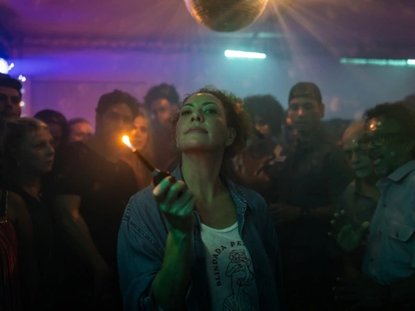 A woman lights up amidst colorful lights and a crowd in Uma Mulher Sem Filtro’s club scene