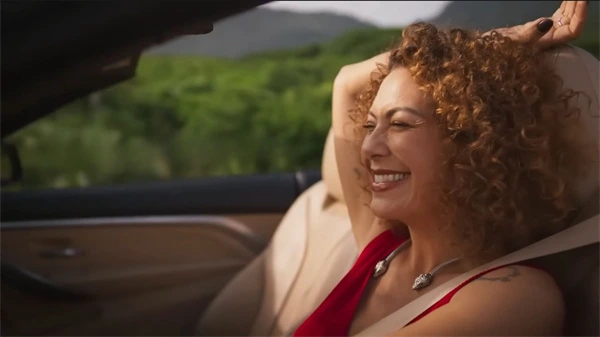 A curly-haired woman grins joyfully while riding in a convertible in Uma Mulher Sem Filtro