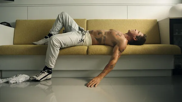Tattooed racing driver rests shirtless on a couch in "F1 The Movie".