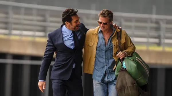 Two men walk and interact in a scene from "F1 The Movie".