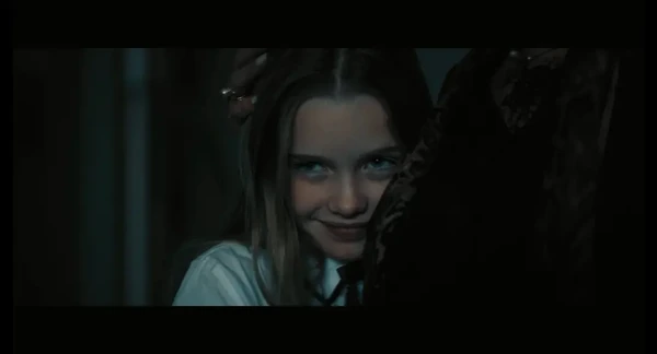 Girl smiling eerily in "Exterminadores do Além Contra a Loira do Banheiro" in dim light.